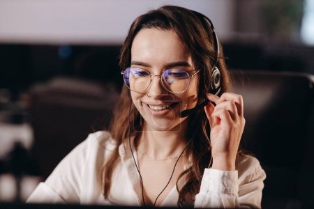 Foto de Call center operator talking to customer with smile. Smiling girl in headset answering clients call. Photo of female support service worker. Hotline operator. High quality photo - Imagen libre de derechos