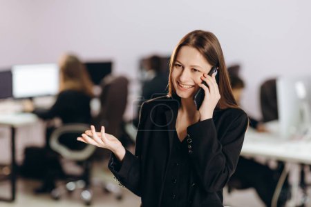 Photo for Joyful female team leader talking on the phone in her office. Beautiful businesswoman making a phone call with smile. High quality photo - Royalty Free Image