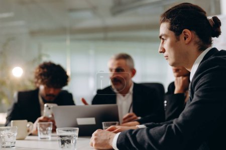 Foto de Business meeting of business partners in the office. A young businessman sits at a table together with partners on a blurred background. High quality photo - Imagen libre de derechos