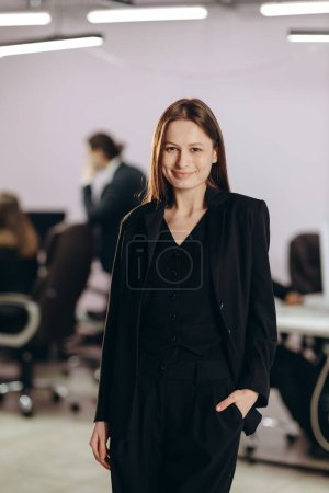 Foto de Hermosa mujer de negocios en traje negro posando en la oficina. Mujer gerente corporativa mirando a la cámara con sonrisa en su lugar de trabajo. Foto de alta calidad - Imagen libre de derechos