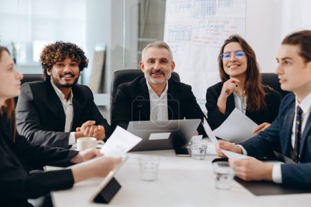 Téléchargez les photos : Une équipe souriante d'investisseurs assis à une table dans un espace de bureau. Partenaires d'affaires assis dans le bureau discutant de nouvelles start-up. Photo de haute qualité - en image libre de droit