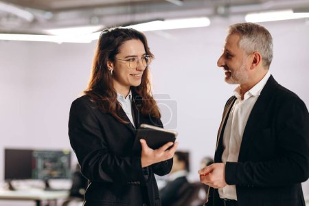 Photo for Smiling businesswoman with tablet talking to company executive. Female manager in glasses having small talk with her boss in the office. High quality photo - Royalty Free Image