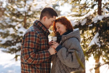 Téléchargez les photos : Couple romantique avec thermos tasse dans le parc d'hiver. Petit ami et petite amie profiter d'un rendez-vous dans la forêt enneigée. Histoire d'amour d'hiver. Photo de haute qualité - en image libre de droit
