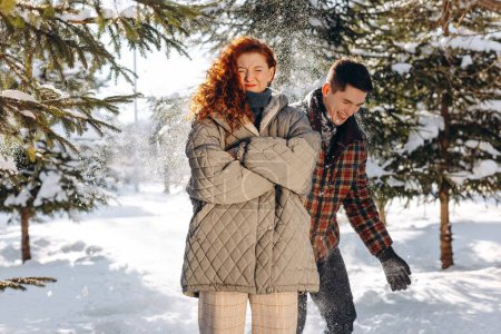 Photo for A young brunette sprinkles snow on his red-haired girlfriend. A man teases his girlfriend while walking in a winter sunny forest. High quality photo - Royalty Free Image