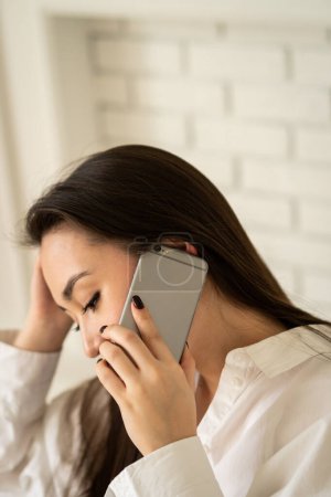 Foto de Una joven morena se sienta con un teléfono en la oreja. Una guapa morena está hablando por teléfono con sus amigas. Foto de alta calidad - Imagen libre de derechos
