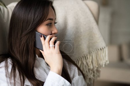 Foto de Una mujer de pelo largo y oscuro está hablando por teléfono. Vista de una joven morena sentada en una silla con un teléfono y llamando a alguien. Foto de alta calidad - Imagen libre de derechos