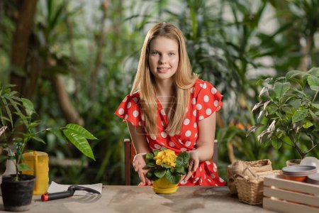 Foto de Una mujer con guantes de jardinería mira a la cámara y sonríe. Chica rubia plantando semillas en la olla. Gran jardín - Imagen libre de derechos