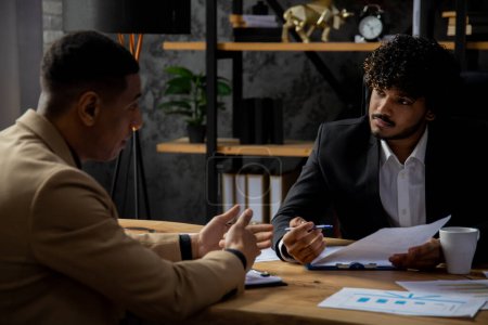 Photo for Two entrepreneurs are sitting at a table discussing ideas for a new startup. Men in strict business suits sit in the office and study various documents. High quality photo - Royalty Free Image