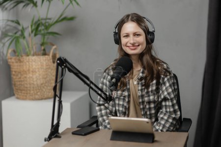 Photo for Indoor shot of smiling girl during podcast. Brunette woman in checkered shirt and headphones during podcast session. High quality photo - Royalty Free Image