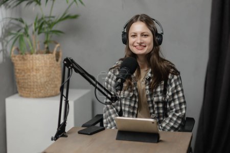 Téléchargez les photos : Une fille souriante dans un casque fait du podcast. Une jeune femme brune travaille à la radio. Photo de haute qualité - en image libre de droit