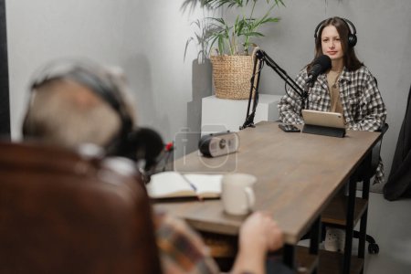 Téléchargez les photos : Deux blogueurs mènent un podcast commun assis dans le studio. Un homme et une femme s'assoient à une table devant les microphones et parlent de quelque chose. Photo de haute qualité - en image libre de droit