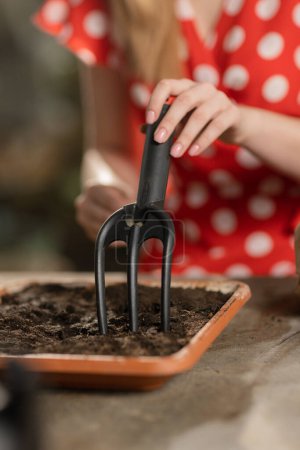 Téléchargez les photos : Une femme en gants de jardinage met de la terre dans un pot de fleurs et y plante des graines. Fille blonde plantant des graines dans le pot. Images 4k de haute qualité - en image libre de droit