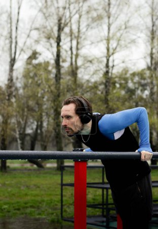 Photo for Man spending free time on sports playground. Preparing for competition. Strong sportsman doing push ups using parallel bars. Adult sportsperson focused on his goals. High quality photo - Royalty Free Image