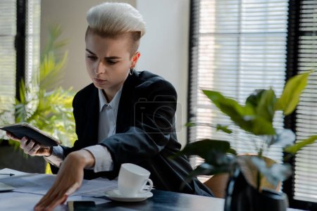Photo for Concept of finance analytics. Serious businesswoman doing reports review. Female executive director with blonde short hair watching papers and holding tablet. High quality photo - Royalty Free Image