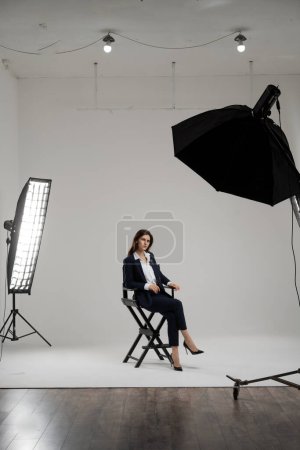 Photo for Young businesswoman sitting chair in photostudio. Business woman posing at studio isolated on white background. Confident self employed lady dressed formal wear photographing. High quality photo - Royalty Free Image