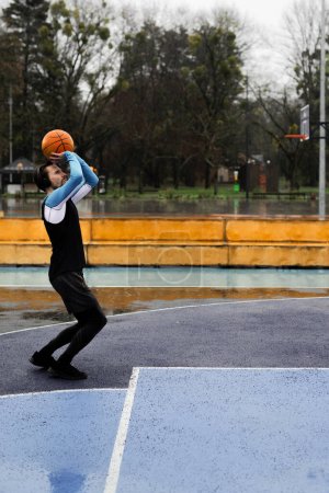 Photo for Concept of healthy lifestyle. Basketball game player. Rainy weather training. Young slim guy throwing ball in ring at sport playground background. Sportsman concentrated on streetball game. High - Royalty Free Image
