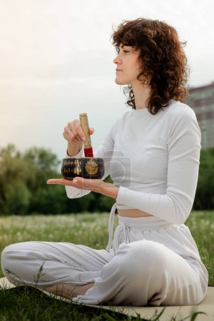 Téléchargez les photos : Une femme yogi tient un bol de chant tibétain antique. Fille assise enseignant la technique de méditation pour renifler les épices. Équilibre complet du chakra dans le corps de la fille. Matériel artisanal traditionnel indien à la satisfaction - en image libre de droit