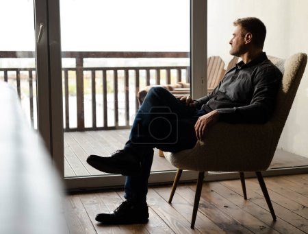 Photo for Shot of a man sitting in the chair behind window terrace. Confident businessman deep thinking looking far away. Male religious prayer waiting jesus christ therapy. High quality photo - Royalty Free Image