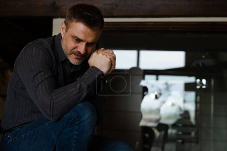 Photo for Alone man sitting at home in depression. Stressed male clasped arms begging god help with problems. Adult daddy praying for his family wellbeing. Human asking jesus christ support. High quality photo - Royalty Free Image