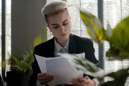 Photo for Serious young woman working with papers in her office. Businesswoman check agreements when sitting alone indoors. Female financial director focused on supply contracts. High quality photo - Royalty Free Image