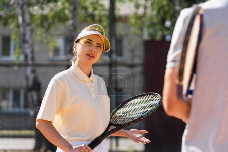 Téléchargez les photos : Joueuse de tennis jeune fille tenant la raquette et écouter les conseils de son entraîneur professionnel. Femme de sport en vêtements de sport tenir raquette sur le court de tennis. Discuter avec l'entraîneur de la concurrence. Haute qualité - en image libre de droit