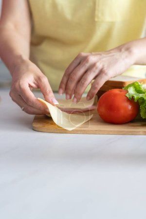 Photo for A young lady prepares sandwiches from fresh vegetables. Woman hand holds a piece of cheese. The concept of healthy eating from natural organic products. Close up. The selective focus mode no face - Royalty Free Image