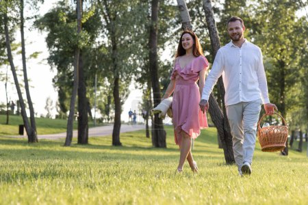 Photo for Couple holding hands while carrying picnic basket on garden background. Young family having a date at local park. Romantic relationships outdoors leisure. Husband invite his wife celebrate anniversary - Royalty Free Image