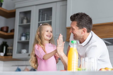 Photo for A friendly family from father with daughter stand and manage in the kitchen. A young serious man dad gives his child culinary instructions to make sandwiches independently. The concept of mutual - Royalty Free Image