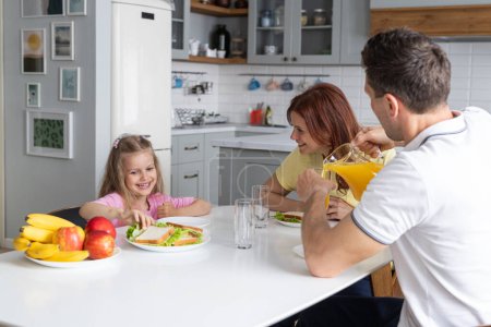 Photo for An american dream friendly family in the kitchen in a joyful mood prepare for lunch together. A young man father and smiling daughter set the table, while mother sits and rests with smartphone. The - Royalty Free Image