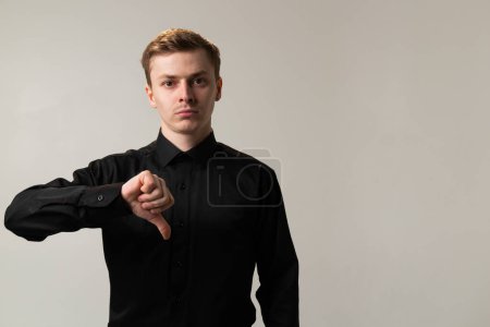 Photo for A man in a black dress shirt is showing disapproval by lowering his thumb near his chin with his arm and sleeve visible. - Royalty Free Image