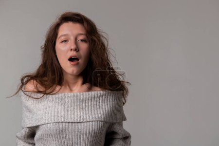 A woman in a sweater is yawning with her mouth open, revealing her layered hair. Despite appearing tired, she is still happy and smiling during the event, adding a touch of fun to her gesture