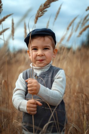 Foto de Moda infantil, estilo retro. Un niño sonriente con un abrigo y gorra de estilo retro se para y sonríe. Copiar espacio. - Imagen libre de derechos