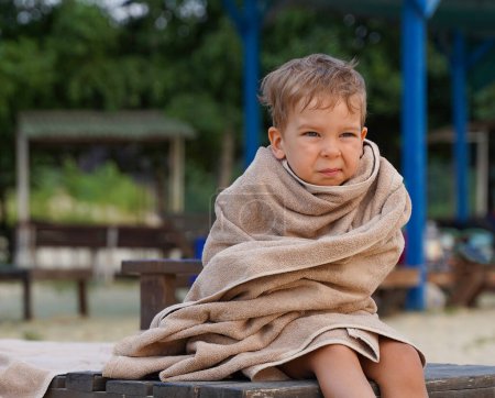 Photo for The little boy wrapped in towel for warming, sad facial expression. A little boy on the seashore - Royalty Free Image