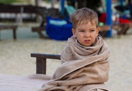Photo for The little boy wrapped in towel for warming, sad facial expression. A little boy on the seashore - Royalty Free Image