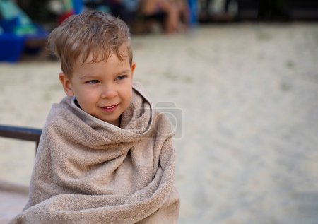 Photo for The baby, wrapped in a towel, is warming himself on a sun lounger by the sea. Baby in anticipation of bathing. - Royalty Free Image