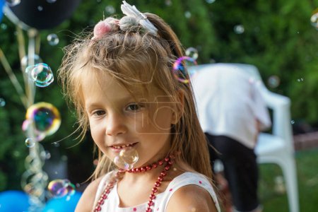 Foto de Retrato de una chica rubia en pompas de jabón. Fiesta de niños en el patio trasero. Entretenimiento verano. - Imagen libre de derechos