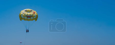 Photo for Parasailing on a yellow parachute against the blue sky. A parachute with a yellow smiling face. Air entertainment. Water sports and fun. Summer vacation at sea. - Royalty Free Image