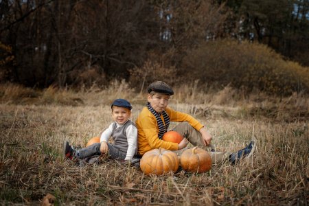 Photo for Two boys in retro clothes sitting in an autumn field. Children and pumpkins. Autumn harvest - Royalty Free Image