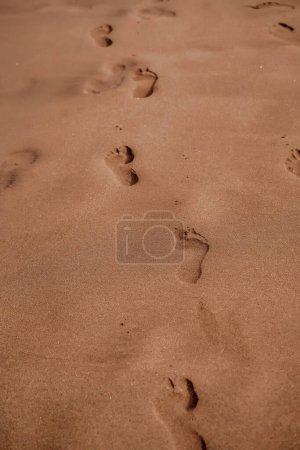 Das Bild fängt eine Spur von Fußabdrücken im weichen, glatten Sand ein und lädt zur Betrachtung eines friedlichen, einsamen Spaziergangs am Strand ein. Fußabdrücke im weichen Sand führen in die Ferne.