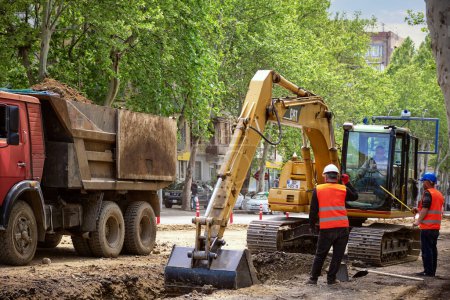 Photo for Public utility workers are replacing the water supply and sewerage system in the city on Tsereteli Avenue. Working excavator on the roadway street: Tbilisi, Georgia - April 23, 2023. - Royalty Free Image