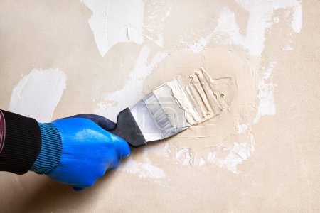 Foto de Un hombre está enyesando una pared dañada en una habitación con una paleta de mano. Do-it-yourself renovación del hogar. - Imagen libre de derechos
