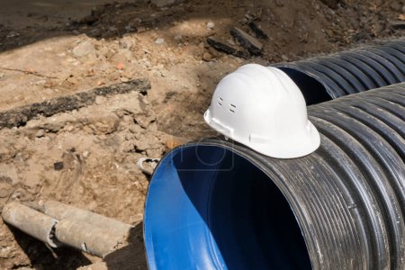 Photo for Close-up of a white plastic safety helmet on a black corrugated pipe. The work of public utilities to improve the infrastructure of the metropolis. - Royalty Free Image