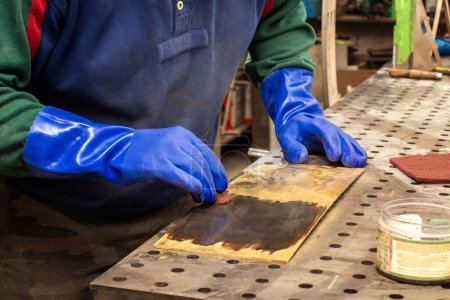 A metalsmith works in his workshop. Production of decorative metal elements. Chemical processing of non-ferrous metals.