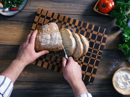 A man cuts Italian Ciabatta bread on a beautiful wooden board. In the home kitchen.