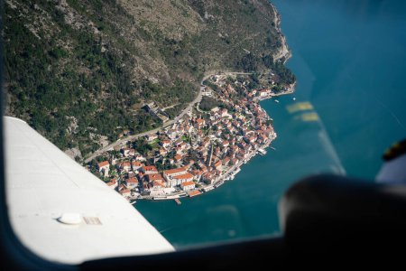 Vista aérea de la ciudad costera y el ala del avión. Fotoperspectiva aérea de alta calidad de una pintoresca ciudad costera enclavada entre montañas y mar, vista desde un ala de aviones. 