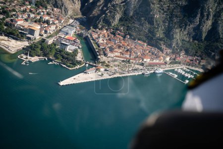 Birds eye view of a picturesque coastal town with historic architecture, nestled between mountains and a marina filled with boats. 