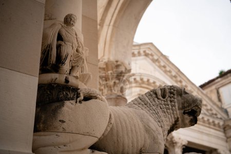 Ein kunstvoll geschnitzter Marmorlöwe neben einer klassischen Figur an der Fassade eines historischen Gebäudes. 