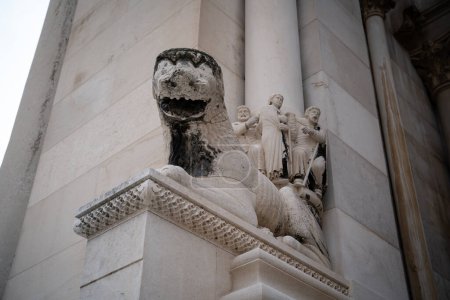 A stone lion sculpture, with a detailed human figures relief in the background, adorns an elegant historic building. 