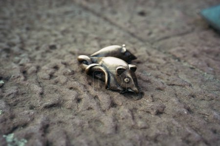 An intricate bronze sculpture of a mouse lies on a textured cobblestone surface, showcasing urban artistic expression. 