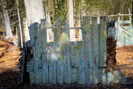 Foto de A base for hiding in Paintball, a fortification behind a wooden wall among trees. A place to play in the woods. - Imagen libre de derechos